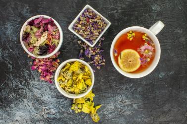 close up photo of herbal tea near bowls of dry flowers on grey background
